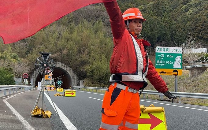 高速道路のトンネル手前で旗を振る警備スタッフ