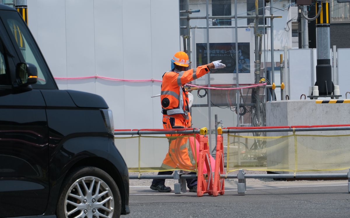 工事現場の前で、手を伸ばして車両を誘導する警備スタッフ
